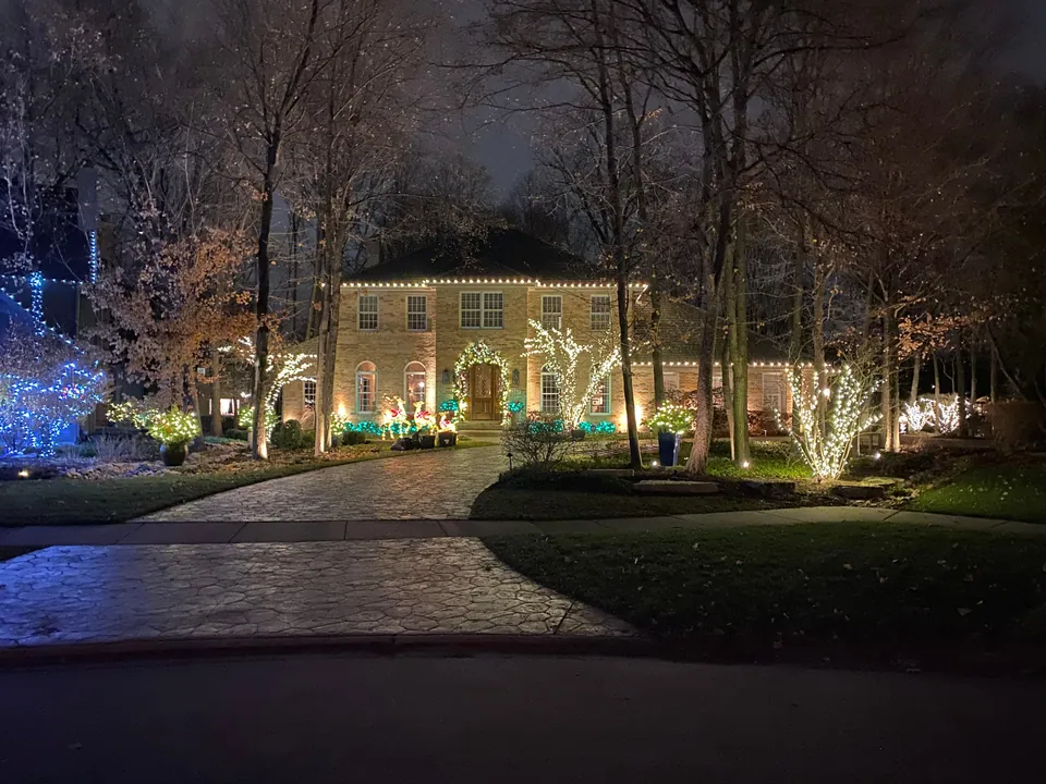 Christmas roofline lights and wrapped trees beside a brick house