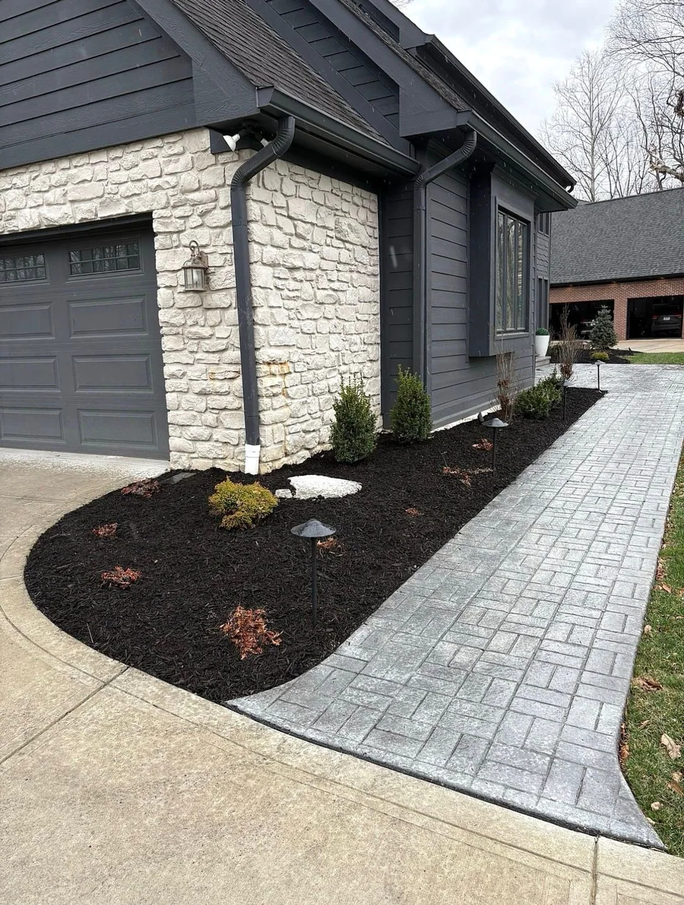 Gray patterned walkway beside a mulched front bed and path lights