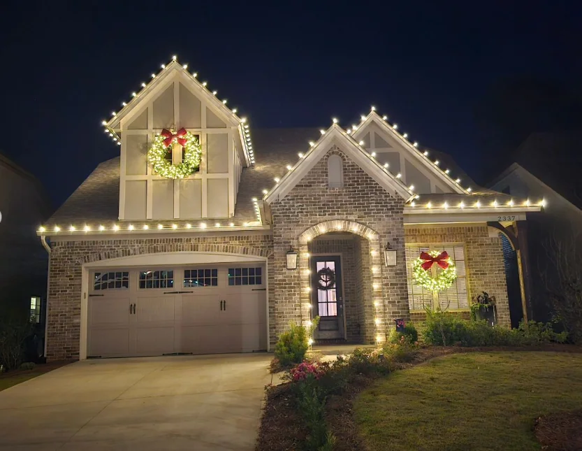 Warm white roofline lights and two wreaths on a brick house