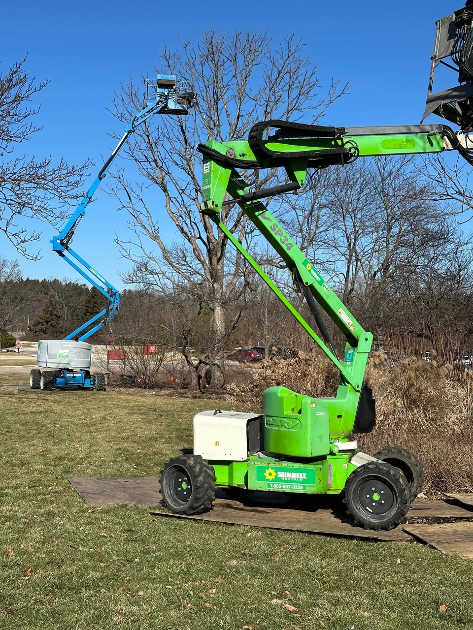 Boom lifts positioned beside tall bare trees