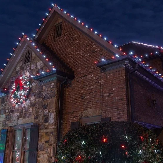 Red and white roofline lights with a wreath on a brick and stone house