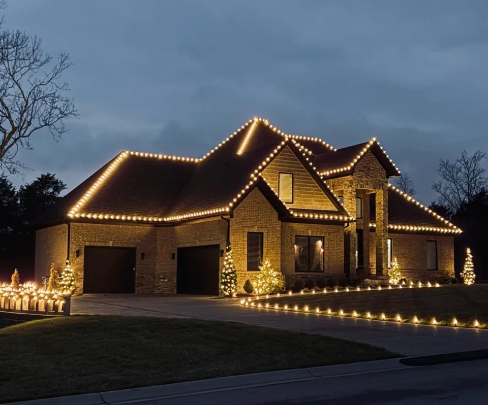 Warm white lights outlining a house roofline and front beds