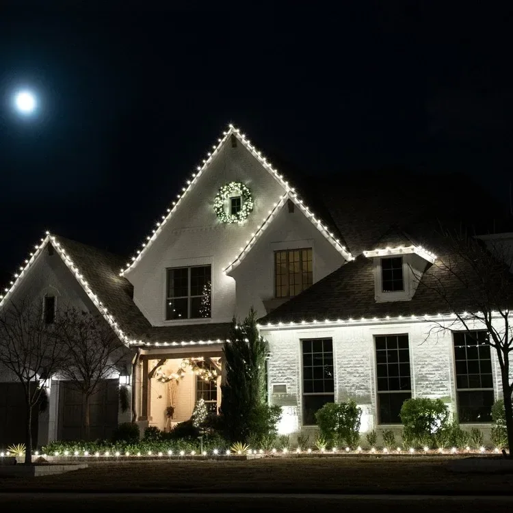 White lights outlining a house roof, walkway and wreath
