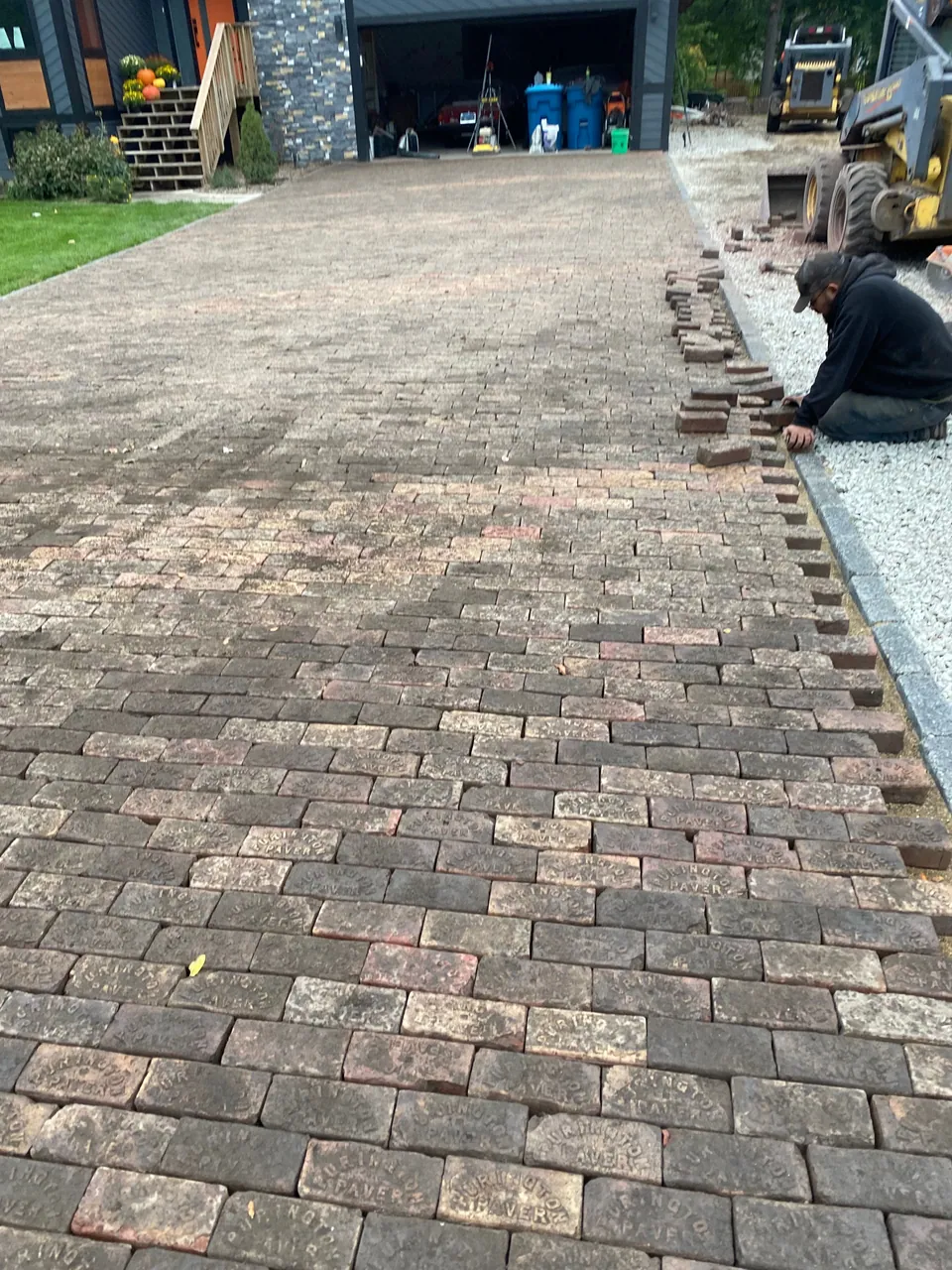 Worker laying pavers along the unfinished edge of a driveway