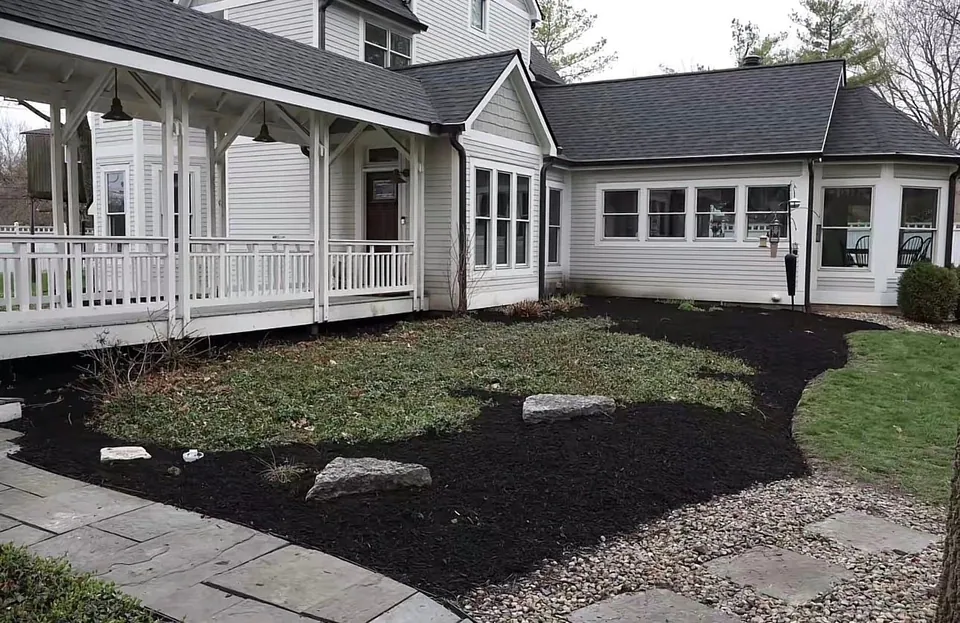 Fresh dark mulch, groundcover and rocks beside a white porch